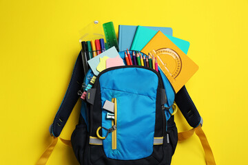 Backpack with school stationery on yellow background, top view