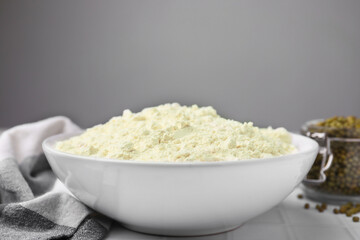 Mung bean flour in bowl and seeds on white tiled table, closeup