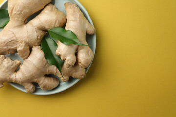Fresh ginger with green leaves on pale light yellow background, top view. Space for text
