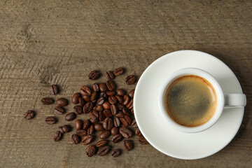 Cup of aromatic coffee and beans on wooden table, flat lay. Space for text