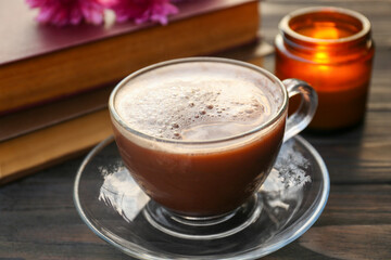 Glass cup with coffee, books and burning candle on wooden table, closeup. Morning ritual