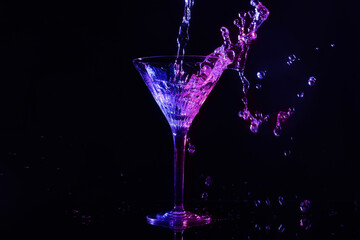 Pouring martini. Glass and splashes in neon lights on dark background