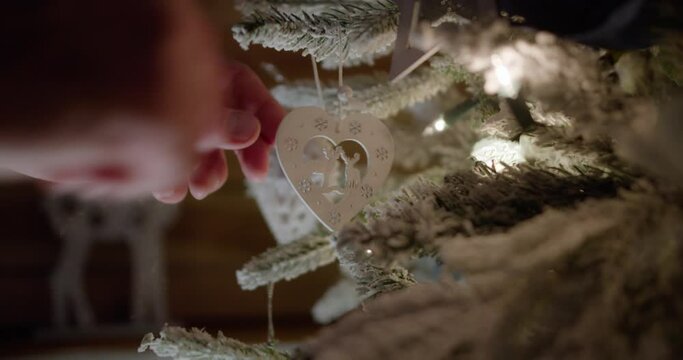 Christmas tree decorating | close-up male hand hangs a heart on a Christmas tree  in the vintage wooden interior |  4k 12-bit raw quality footage | basic color grading