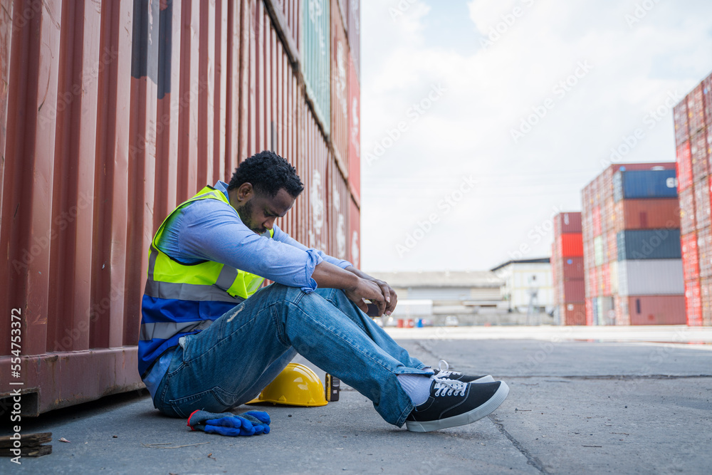 Poster Worker sitting to rest with container wall in background.