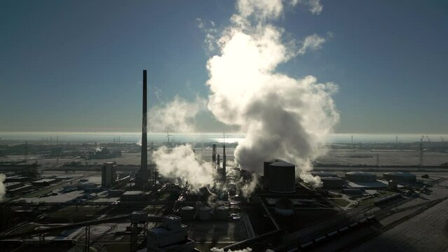 Smoke and steam rising of an industrial facility, CO2 emissions, air pollution, exhaust gases, aerial drone shot, backlit scene, rising moving up