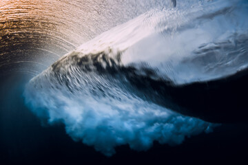 Barrel wave crashing in ocean with sunset or sunrise. Underwater view of surfing wave