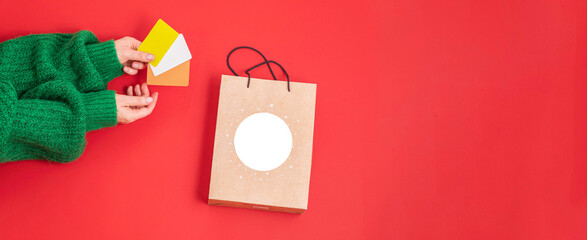 Xmas shopping concept. Woman's hands holding a gift bag and a credit card on a red background,