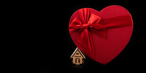 Symbolic wooden miniature house and a large gift box in the form of a human heart on a black background