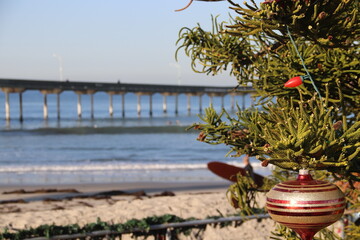 Sunny California Christmas with Christmas tree on the beach next to the surf, surfers and pier in...
