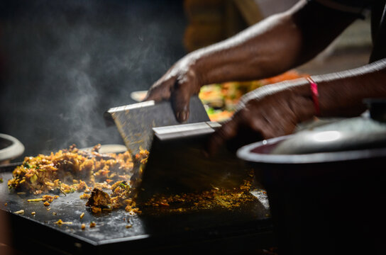 Hands of the kottu roti vendor, making kottu on top of a hot steel grill plate