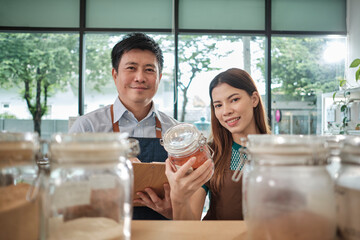 Portrait of two shopkeepers with natural organic products in reusable glass jars, smile and look at camera in refill store, zero waste, plastic-free grocery, and eco-friendly, sustainable business.