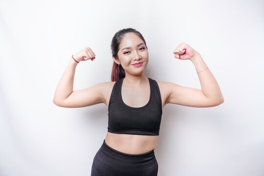 Excited Asian sporty woman wearing a sportswear showing strong gesture by lifting her arms and muscles smiling proudly