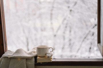 Cozy winter still life. Cup of hot tea and an open book with a warm sweater on a vintage wooden...