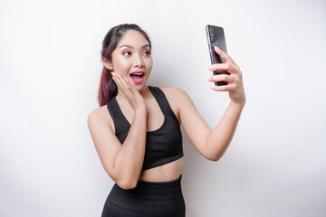 Naklejka premium A portrait of a sporty Asian woman wearing a sportswear and holding her phone, isolated by white background