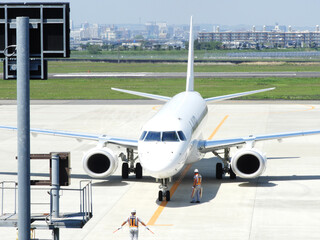 夏の宮崎空港に駐機する旅客機エンブラエル190と誘導するマーシャラー