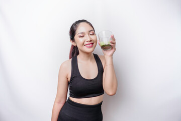 Joyful sporty Asian woman wearing sportswear with glass of tasty green smoothie, isolated on white background.