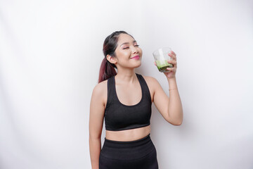 Joyful sporty Asian woman wearing sportswear with glass of tasty green smoothie, isolated on white background.