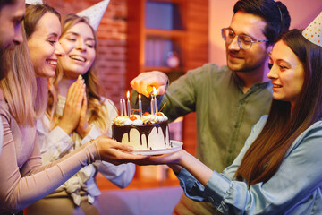 Friends standing together, holding a plate with a cake and celebrating birthday