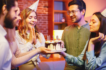 Friends standing together, holding a plate with a cake and celebrating birthday