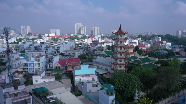Buddhist temple and prayer tower in urban rooftop setting with view to city skyline on a sunny day with blue sky. Location is An Phu in Ho Chi Minh City, Vietnam. Drone ccw orbit with cell tower.