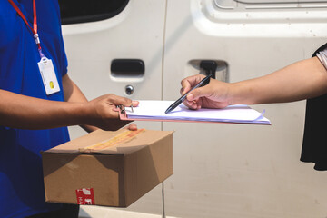 Customer signing on document while courier giving package, close up hands.