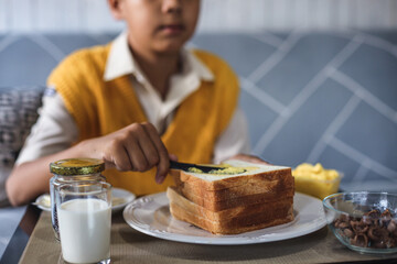 Blurry image of Asian school boy in uniform making bread toast at the kitchen during breakfast time.