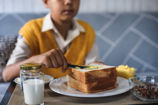 Blurry Image Of Asian School Boy In Uniform Making Bread Toast At The Kitchen During Breakfast Time.