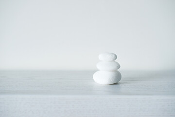 Pyramid of white pebble meditation stones on white wooden table on a white background. Zen Concept of harmony, balance and meditation. Pile of balanced rocks or stones on wooden table