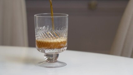 Dark beer is poured into glass on white glass table in kitchen