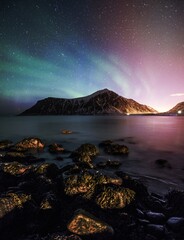 Fototapeta na wymiar Aurora borealis with stars over mountain with rock on coastline
