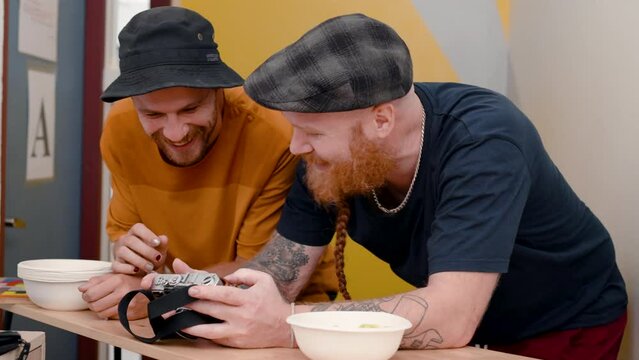 4K, Two male tourists who are best friends are standing at the counter in hostel's living room. Scrolling through pictures from the camera that have been taken from tourist attractions.