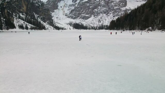 Tourists Walking On Frozen Lake Braies During Winter In Trentino, Italy. Majestic Mountains Revealed In Background. tilt-up