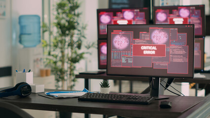 Computers displaying critical error message flashing on screen, dealing with hacking threat and computer malware. Empty desk with multiple monitors showing security breach alert.