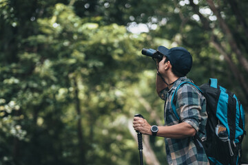 Hikers use binocular to see animals and view landscape  with backpacks walking through on the road in the forest. hiking and adventure concept.