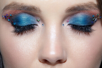 Closeup shot of human woman face with eyes closed and beauty makeup with blue eye shadow make up...