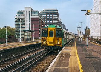 Naklejka premium British passenger train arriving at platform; railroad tracks and platform in foreground; residential buildings in background