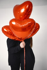 Man and woman kissing covering with bunch of heart-shaped red ballons