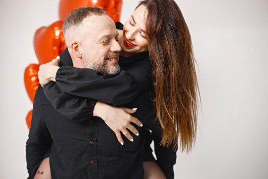 Man carrying woman piggyback while posing in studio near bunch of heart-shaped red ballons