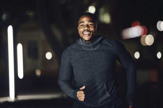 Runner, health or fitness black man at night running in city, street or road for marathon training, race event or workout. Happy, smile or sports athlete for wellness exercise, goal target or success