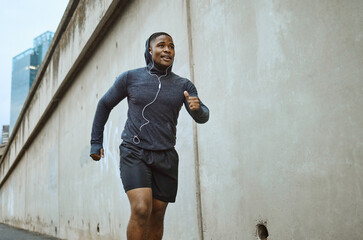 Black man, fitness and running in the city with earphones listening to music during cardio workout. Active African American man runner enjoying audio track, healthy exercise or training in urban town - obrazy, fototapety, plakaty