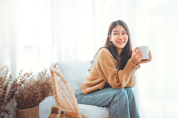 Happy asian woman relaxing drinking hot coffee or tea in holiday morning vacation on armchair at home, Cosy scene, Smiling pretty woman drinking hot tea in autumn winter. copy space.