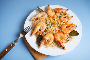 Funchosa is a dish of Korean cuisine with shrimp on a white plate and on a blue background with a fork.