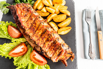 top view of the delicious juicy grilled pork ribs with potato slices and salad on a slate board. Cutlery. delicious food.