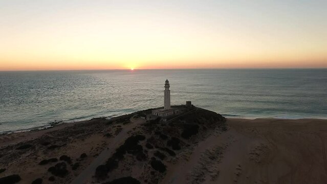 Drone approaching the Lighthouse as the sun sets in the Calm water at the horizon at Cadiz coast Spain