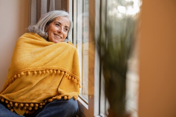 elderly woman with blanket at home looks out the window, a cold day