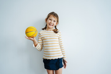 Cheerful little girl posing for a photo, holding a mini basketball on her hand