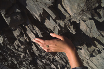 Close up female hand touching basalt rock concept photo. Nature beauty. First person view photography with black stone on background. High quality picture for wallpaper, travel blog, magazine, article