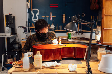 Focused artisan craftsman brushing cello in workshop