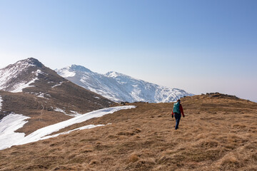 Rear view of woman with backpack looking at snow capped mountain peak Zirbitzkogel and Kreiskogel, Seetal Alps, Styria (Steiermark), Austria, Europe. Hiking trail Central Alps in sunny early spring