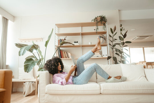 Happy Woman Using Laptop Lying On Sofa In Living Room